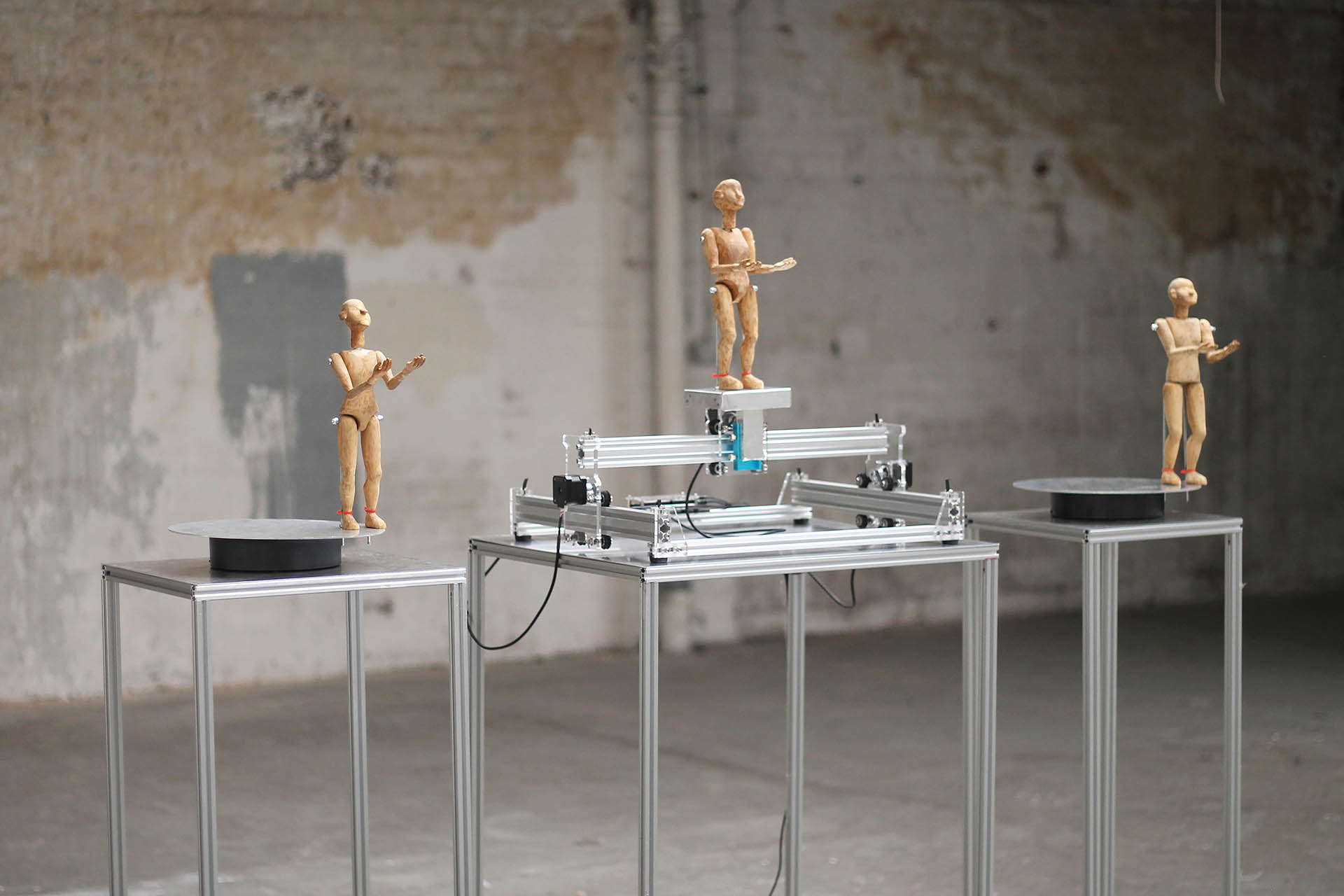 3 wooden human puppets sit on top of 3 metal stand